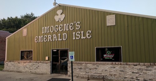 Exterior of Imogene's Emerald Isle, a green building with a sign featuring a shamrock, located in a small town.