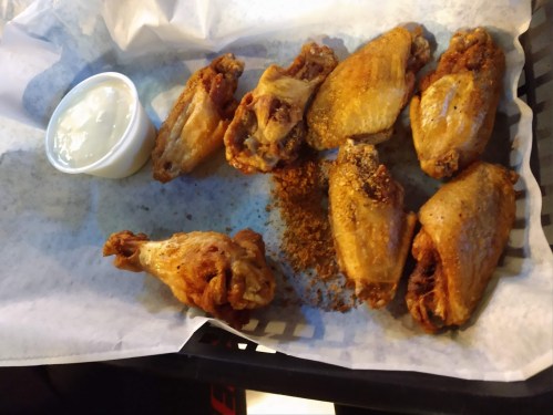 A plate of crispy chicken wings with a side of dipping sauce on a checkered paper.