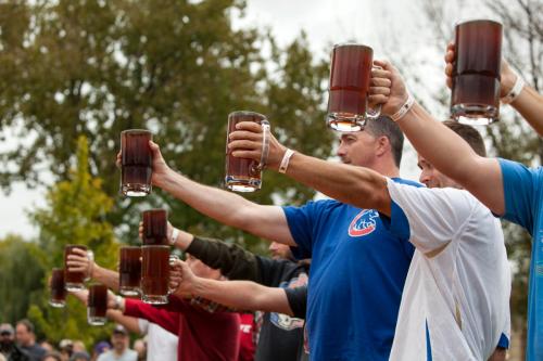 A group of people raising large mugs of dark beverages in a festive outdoor setting.