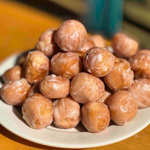 A plate piled high with glazed doughnut holes, golden brown and shiny, set against a blurred background.