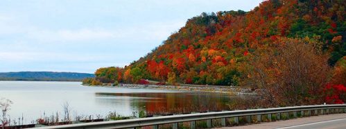 Scenic view of a lake surrounded by vibrant autumn foliage and a winding road along the shore.