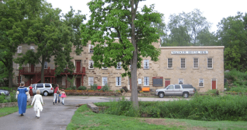A stone building with multiple windows and a sign reading "Mansfield House" surrounded by trees and a pathway.