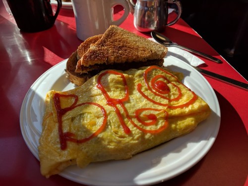 A plate with a ketchup-decorated omelette and toasted bread, set on a red table.