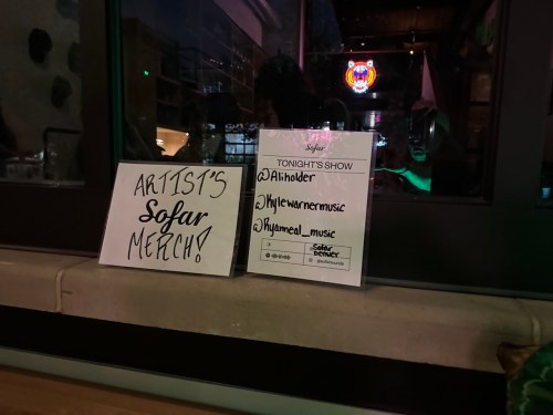 Sign promoting artist merchandise for a Sofar show, featuring social media handles and event details.