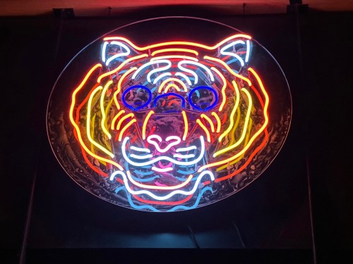 Colorful neon sign of a tiger wearing blue glasses, set against a circular background.