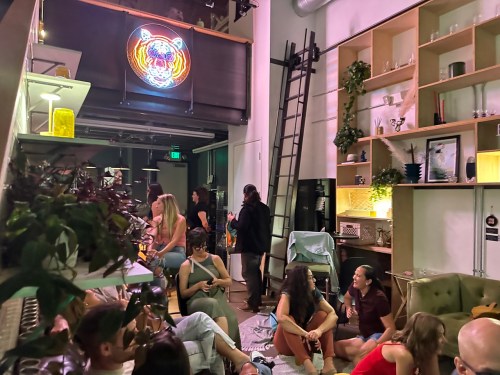 A lively indoor space with people socializing, a neon tiger sign, and plants decorating the area.