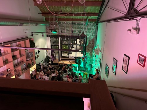 A view from above of a lively gathering in a venue with green lighting and a stage, filled with seated attendees.