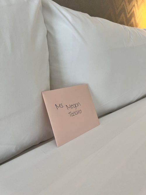 A pink envelope addressed to "Ms. Megan Tataro" resting on a neatly made bed.