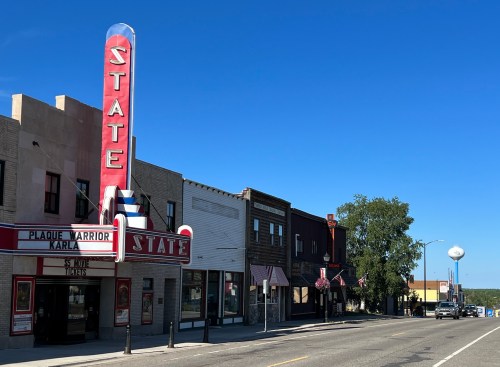 A vintage theater with a bright marquee stands alongside historic buildings on a clear day in a small town.