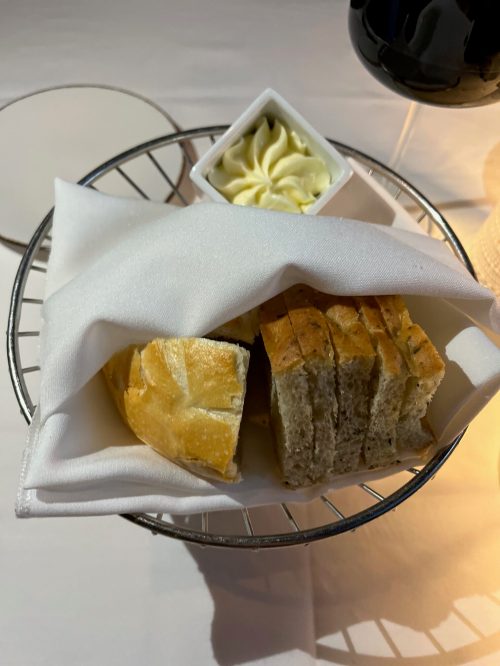 A basket with sliced bread and a small dish of butter, covered with a white napkin.