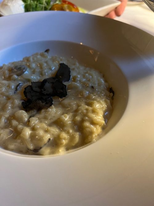 A close-up of creamy risotto topped with black truffle, served in a white bowl.