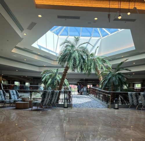 Bright atrium with palm trees, marble flooring, and a skylight, creating a spacious and inviting atmosphere.