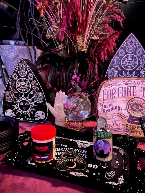 A mystical display featuring tarot cards, a crystal ball, and decorative items on a table with a floral backdrop.