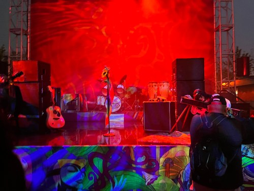 A vibrant stage setup with instruments and colorful murals, illuminated by red lighting, ready for a performance.