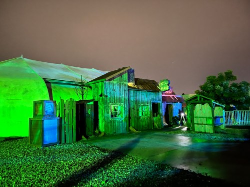 A spooky, illuminated outdoor scene featuring a rustic building and fence under a night sky with green lighting.