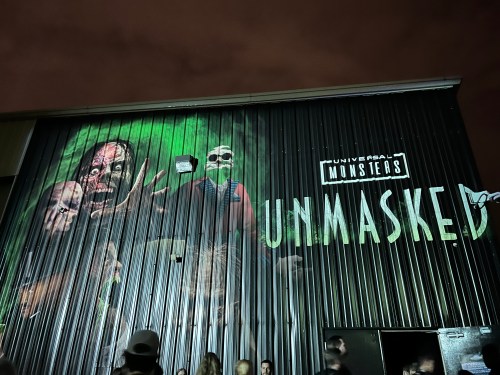 A dark building features a mural of monsters with the text "Universal Monsters Unmasked" illuminated on the wall.