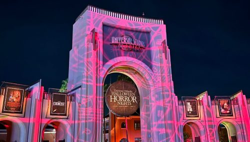 Universal Studios entrance illuminated with Halloween Horror Nights projections, featuring guests in the foreground.