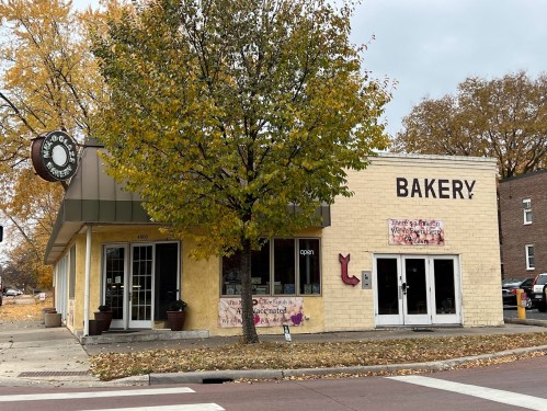A cozy bakery with a yellow exterior and large windows, surrounded by autumn trees and fallen leaves.