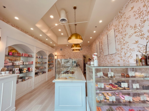 Bright bakery interior with floral wallpaper, display cases of pastries, and golden pendant lights.