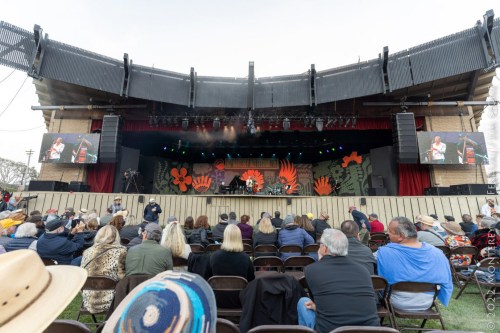 A live music performance on stage with a crowd seated in front, surrounded by colorful decorations.