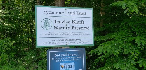 Sign for Trevlac Bluffs Nature Preserve by Sycamore Land Trust, surrounded by greenery, with contact information and a fact box.