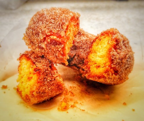 Three golden, sugar-coated cake bites stacked on parchment paper, showcasing a fluffy interior.