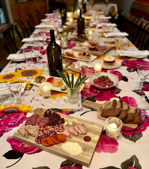 A beautifully set dining table with a floral tablecloth, featuring various dishes, wine bottles, and candles.