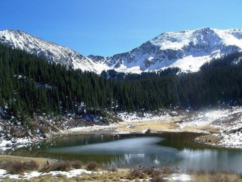 A serene mountain landscape featuring a calm lake surrounded by snow-capped peaks and lush green forests.