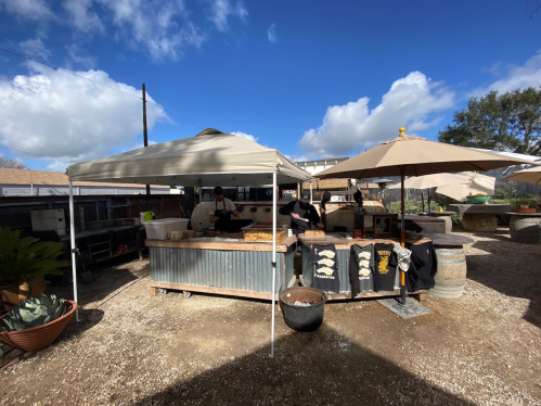 Outdoor food stall with tents, tables, and umbrellas under a partly cloudy sky.
