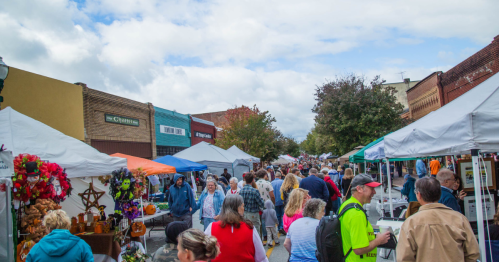 A bustling street market with vendors under tents, colorful decorations, and a crowd of people enjoying the event.