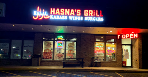 Exterior of Hasna's Grill at night, featuring neon signs for halal kababs, wings, and burgers, with an "Open" sign.