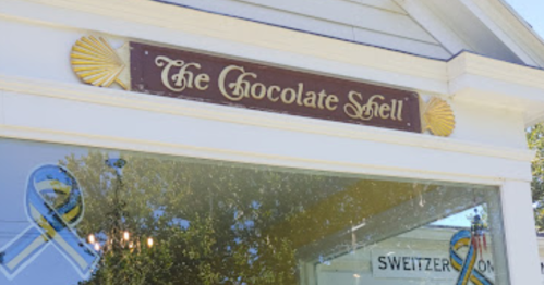 Sign for "The Chocolate Shell" shop, featuring decorative elements and a window display.