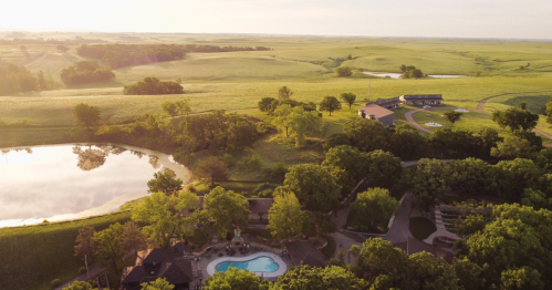 Aerial view of a serene landscape featuring a pool, lush greenery, and a tranquil pond surrounded by rolling hills.