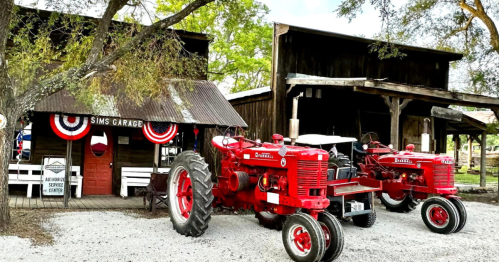 Two vintage red tractors parked outside a rustic garage adorned with patriotic decorations.