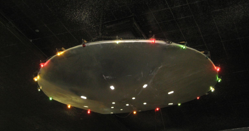 A circular metallic object with colorful lights hanging from a dark ceiling.