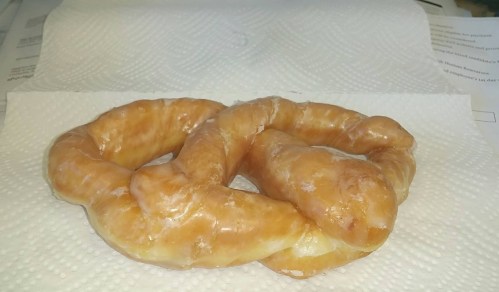 A glazed pretzel resting on a paper towel, showcasing its twisted shape and shiny surface.