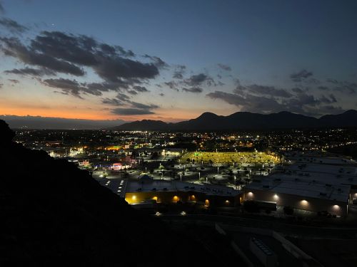 A panoramic view of a city at dusk, with lights twinkling and mountains silhouetted against a colorful sky.