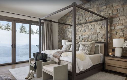 Cozy bedroom with a four-poster bed, stone wall, and large windows overlooking a snowy landscape.