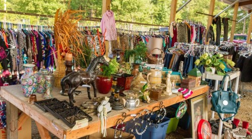 A vibrant outdoor market stall filled with clothing, vintage items, and decorative objects on a wooden table.
