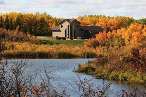 A serene landscape featuring a modern building surrounded by vibrant autumn foliage and a calm lake.