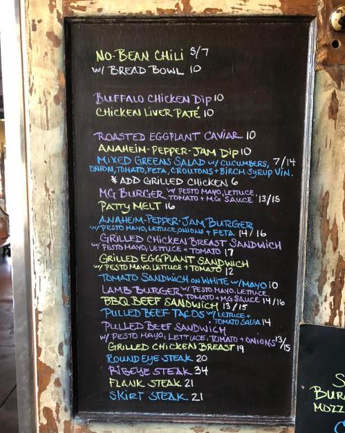 Menu board featuring various dishes and prices, including chili, chicken dip, burgers, and steak options.