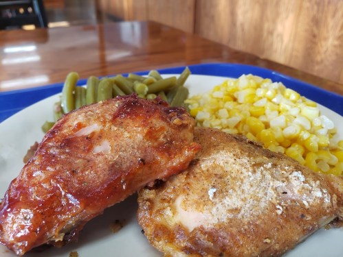 A plate with two pieces of chicken, green beans, and corn, served on a blue dish with a wooden background.