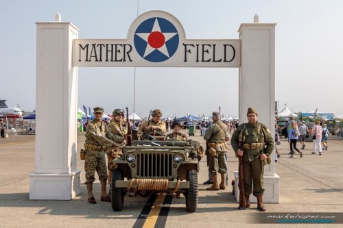 Historical reenactors in military uniforms pose by a vintage jeep under the Mather Field sign at an airshow.