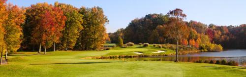 A scenic golf course surrounded by vibrant autumn foliage and a calm lake under a clear blue sky.