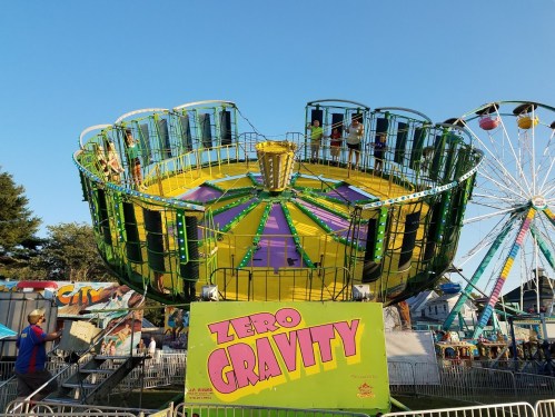 A colorful amusement park ride named "Zero Gravity" with people inside, set against a clear blue sky.