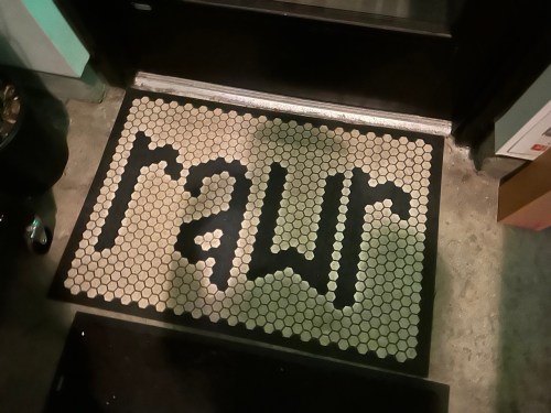 A doormat with the word "rawr" in bold letters, made of hexagonal tiles, at the entrance of a building.