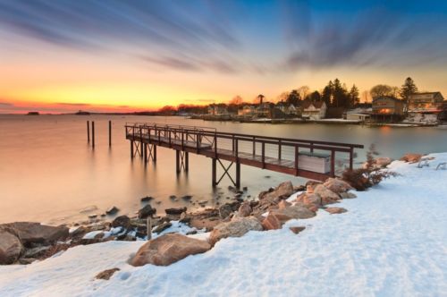A serene sunset over a snowy shoreline with a wooden pier extending into calm waters.