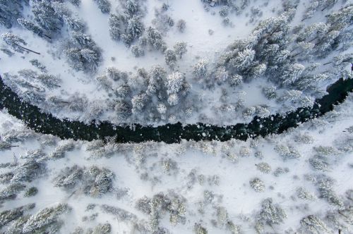 Aerial view of a snow-covered landscape with a winding river surrounded by frosted trees.