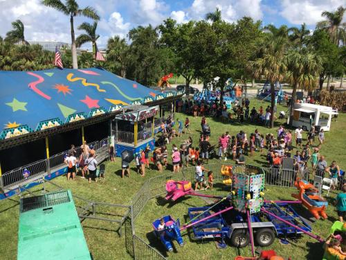 A vibrant carnival scene with rides, a colorful tent, and a crowd of people enjoying the festivities in a park.