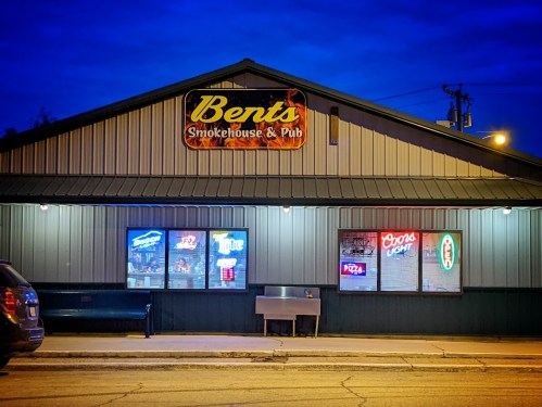 Exterior of Bents Smokehouse & Pub at night, featuring illuminated signs and a bench outside.